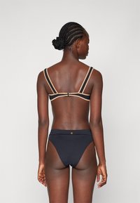 Μαύρο μπικίνι σετ με δίχρωμο σχέδιο, διαθέτει μπεζ ιμάντες και κούμπωμα στο πίσω μέρος. Σαλοπέτα με ψηλή μέση και διακριτική λεπτομέρεια λογότυπου.