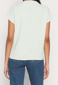 Top verde chiaro a maniche corte con una vestibilità rilassata, scollatura rotonda e texture foderata, abbinato a jeans in denim blu.