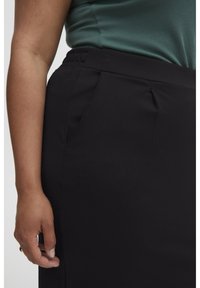 Zwarterok met een gladde textuur, voorzien van zijzakken en een platte tailleband. De stof lijkt rekbaar en comfortabel.