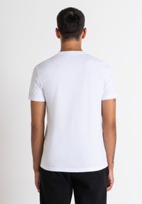 Camiseta de algodón blanca con mangas cortas, escote redondo y diseño ajustado. Textura suave, sin patrones ni adornos. Vista trasera.