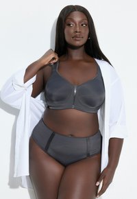 Szary biustonosz i majtki z wysokim stanem wykonane z gładkiej, miękkiej tkaniny z kontrastowymi przeszyciami, zestawione z białą, zapinaną na guziki koszulą.