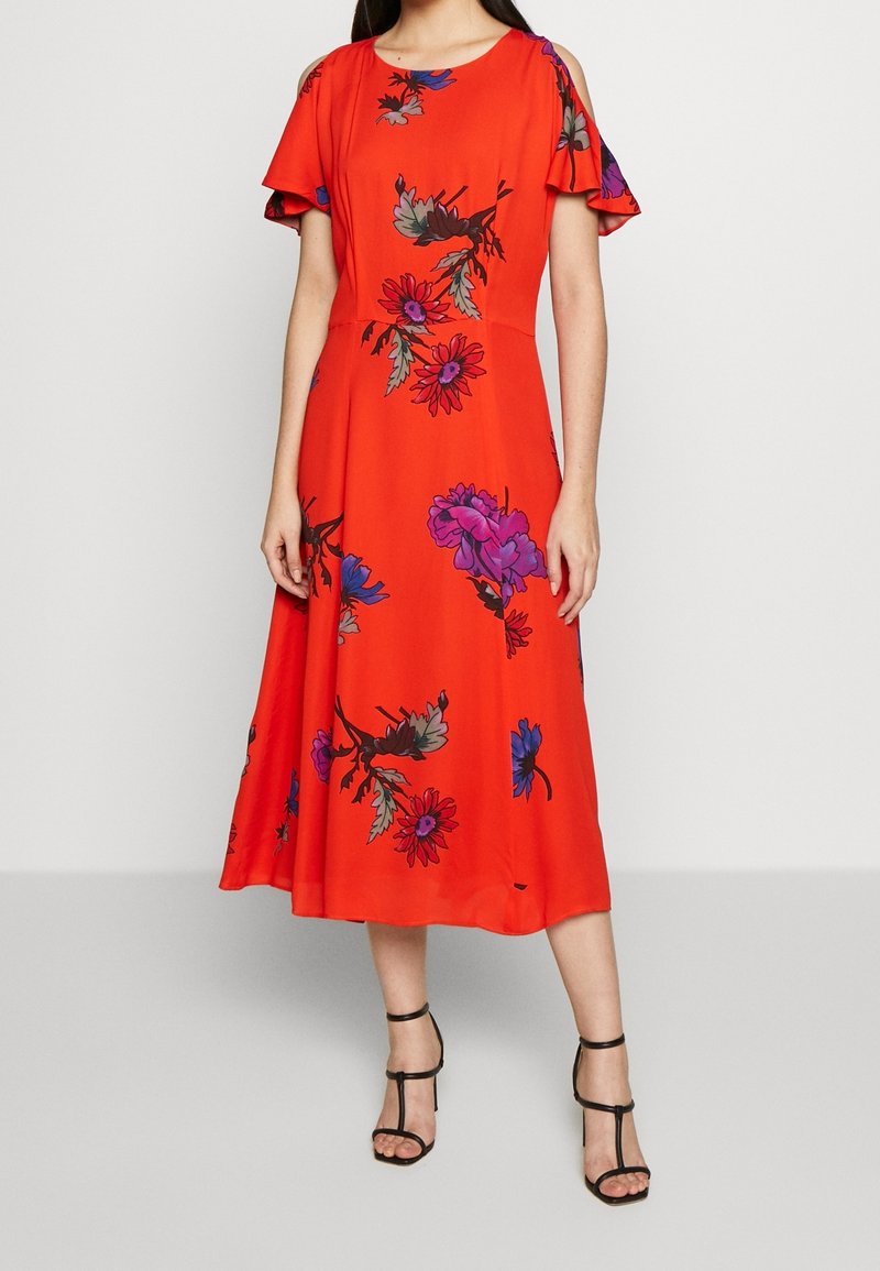 Robe midi rouge avec manches courtes à volants et motifs floraux en violet et bleu. Tissu léger, cintrée à la taille, jupe fluide.