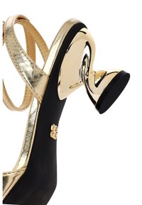Gouden sandalen met hoge hakken en bandjes, met een gebogen metallic hak, zwarte zool en een decoratieve accent aan de zijkant. Gladde textuur en glanzende afwerking.