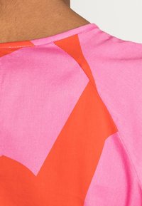 Top colorido con una tela rosa y patrones naranjas angulares y audaces. El diseño tiene una textura suave con costuras visibles a lo largo de las uniones.