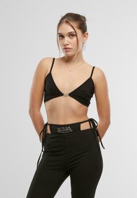 Musthave muströöpidega must crop-top, millel on sügav kaelus ja hõbedane aktsent, koos kõrge vöökohtaga mustade pükstega, millel on külgedel lõiked ja logo detail.