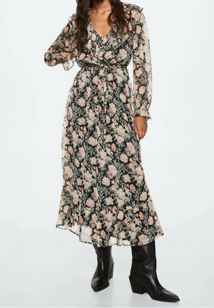 Zwarte bloemenmaxi-jurk met roze en groene patronen. Voorzien van lange, doorschijnende mouwen, een getailleerde taille en een vloeiende zoom. Draagt zwarte laarzen.