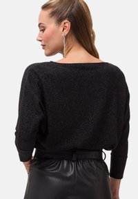 Schwarzer strukturierter Pullover in lässiger Passform mit weitem Halsauschnitt und langen Ärmeln, kombiniert mit schwarzen hochgeschnittenen Hosen aus Kunstleder.