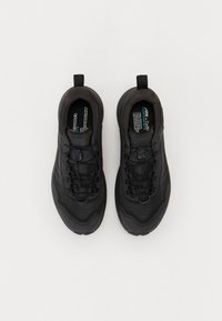 Chaussures de sport noires avec un dessus texturé, dotées de lacets, d'une languette et d'une semelle rembourrée. Logo notable et étiquette de taille visibles à l'intérieur.