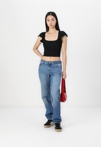 Top corto negro con mangas rizadas, vaqueros rectos de color azul claro, zapatillas negras con suelas beige y un pequeño bolso rojo.