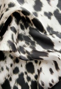 Black and white animal print fabric, smooth texture, featuring irregular spots on a cream background, gently draped to show folds.