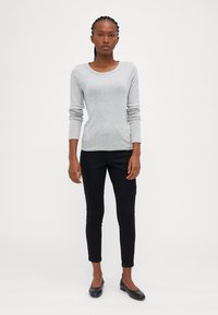 Sweater cinza de manga longa, com gola redonda, combinado com calças pretas ajustadas e sapatilhas pretas. Textura suave, design simples, sem padrões.