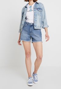 Světlemodrá džínová bunda, bílá tričko s grafikou, modré krajkové šortky s vysokým pasem a sv ětlemodré tenisky. Neformální letní outfit.