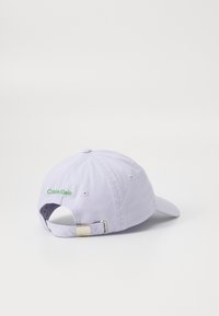 Lilac kokvilnas beisbola cepure ar regulējamu aizmugurējo jostu, metālu sprādzi un zaļu "Calvin Klein" izšūtu logo sānos.