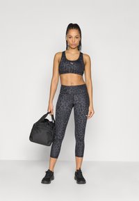 Μαύρο αθλητικό σουτιέν και κολάν με διακριτικό μοτίβο λεοπάρ, συνοδευόμενα από μαύρη τσάντα γυμναστηρίου. Τα παπούτσια είναι μαύρα αθλητικά.