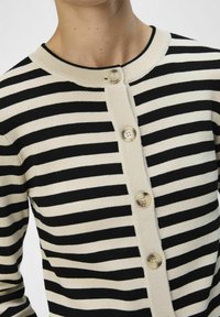 Schwarz-weiße gestreifte Strickjacke mit rundem Ausschnitt und fünf Knöpfen vorne. Das Material wirkt weich und hat eine figurbetonte Passform.