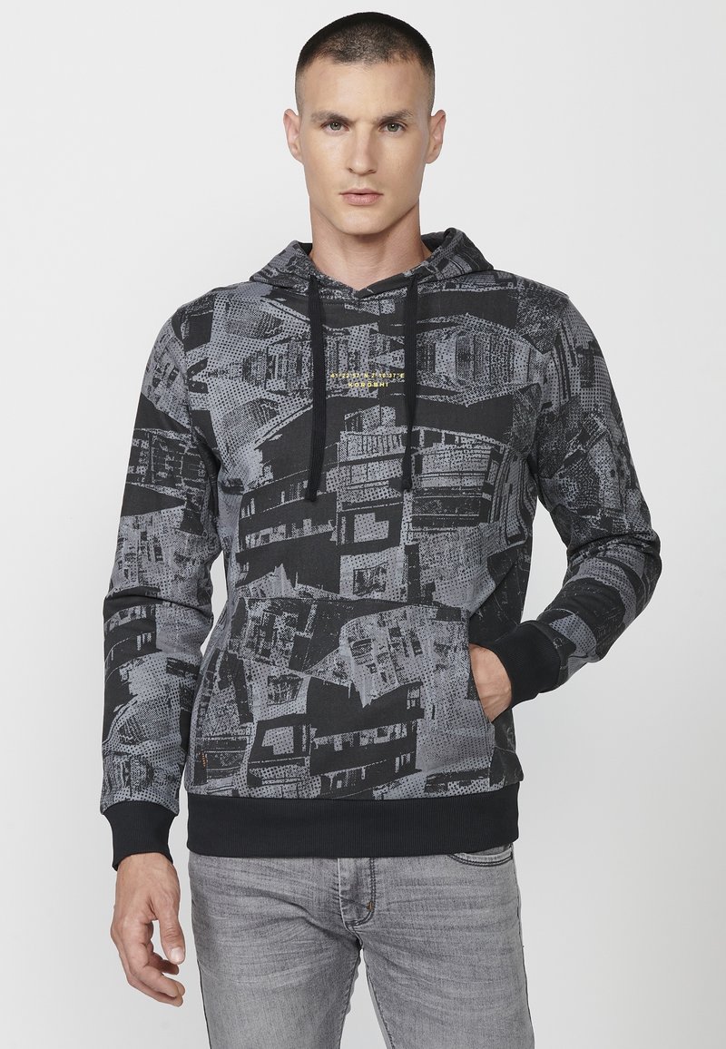 Hoodie u crno-sivoj uzorku s kapuljačom na vezanje, prednjim džepom i rebrastim manžetama. Sadrži geometrijski dizajn s različitim teksturama.