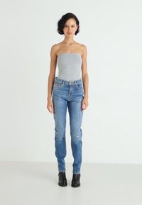 Jeans blu a vita alta con dettagli strappati, materiale in denim, slim fit e un classico design a cinque tasche. Indossati con un top grigio e stivali neri.