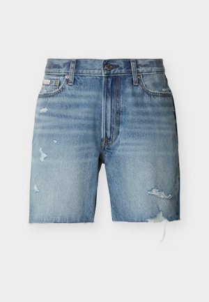 Gaiši zili džinsa šorti ar saplēstām malām, nodiluma detaļām abās kāju pusēs, priekšējo pogu aizdari un priekšējām kabatām uz balta fona.