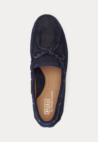 Mørkeblå suede moccasin med lærreimer, dekorative dusk, kontrasterende søm og en tan skinninnersåle med merkevarelogo.