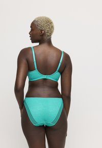 Reggiseno in pizzo turchese con slip coordinati. Il reggiseno presenta spalline regolabili e chiusura a gancio. Texture liscia con dettagli floreali.
