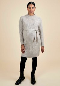 Hellgraues gestricktes Kleid mit einem strukturierten Zopfmuster, ausgestattet mit einem gebundenen Taillengürtel und langen Ärmeln, kombiniert mit schwarzen Stiefeletten und Leggings.