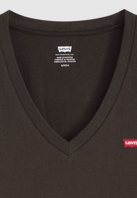 T-shirt noir marron en coton doux à col en V ; présente un petit patch du logo rouge Levi's sur la poitrine ; étiqueté avec des instructions d'entretien.