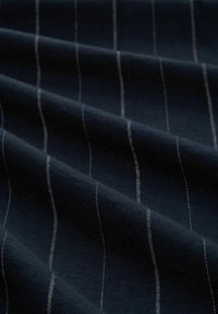 Tessuto blu navy con una morbida textura, caratterizzato da sottili strisce bianche verticali che creano un sottile contrasto contro lo sfondo scuro.
