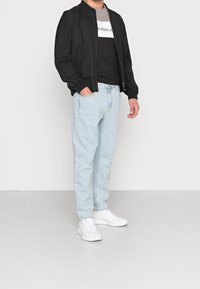 Svart bomberjacka, grå och svart grafisk t-shirt, ljusblå jeans och vita sneakers. Avslappnad outfit med en lös passform.