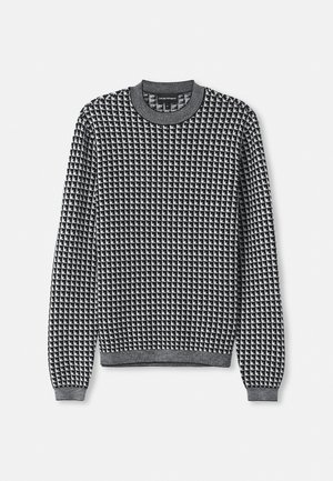 Pull rayé noir et blanc avec un col rond, des manches longues et des poignets côtelés. La texture semble tricotée avec un motif géométrique.