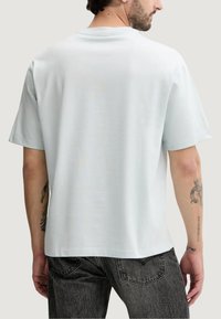 Jasnoniebieska bawełniana koszulka z krótkimi rękawami, okrągłym dekoltem i luźnym krojem. Charakteryzuje się gładką teksturą i brakiem widocznych wzorów.