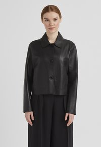 Schwarze Ledermotorradjacke mit rundem Kragen, ausgestattet mit einer vorderen Druckknopfschließe und zwei großen aufgesetzten Taschen. Glatte Textur, minimalistisches Design.