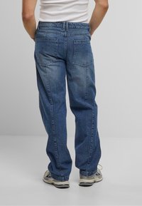 Blå denim jeans med en avslappet passform, som har to baklommer og høy midje. Stoffet ser teksturert ut med subtil falming på bena.