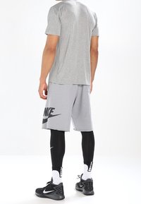 Camiseta deportiva gris de manga corta, combinada con pantalones cortos grises que presentan un logo negro de Nike, mallas ajustadas negras y zapatillas negras.