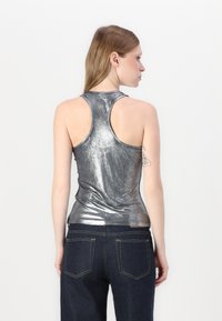 Silver metallisk linne med en figurnära design, racerback-snitt och slät yta, tillsammans med mörkblå jeans med synliga söm detaljer.