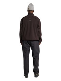 Personne portant une veste noire avec "ATW" dans le dos, un pantalon noir, un bonnet gris et des chaussures noires, debout de dos sur fond blanc.