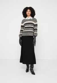 Pleteni pulover s črnimi, kremnimi in sivimi črtami; kombiniran s črno naborkano krilo in črnimi visokimi škornji s petami do kolen; dodatki vključujejo rokavice.