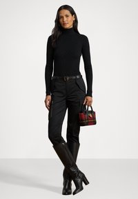 Melna augsta apkakles džemperis, pieguļošas melnas bikses ar sānu rāvējslēdzējiem, melnas ceļu garuma zābaki un maza pārklājuma soma ar dzelteniem akcentiem.