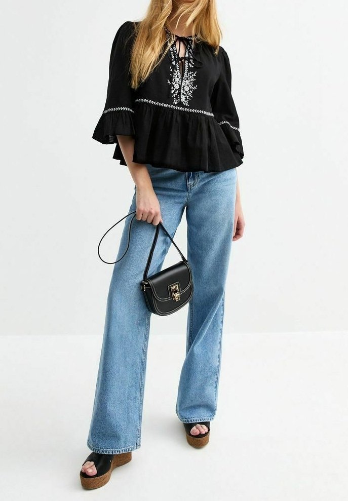 Schwarzes Peplum-Top mit floraler Stickerei, blaue weitgeschnittene Jeans, schwarze Handtasche und Plattformsandalen. Strukturierten Stoff, ausgestellte Ärmel.