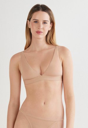 Nude bra with a plunging neckline and thin straps. Soft, smooth material with a seamless design. Minimalistic band under the bust.