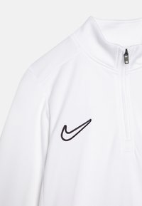 Pull-over blanc Nike avec zip et col montant, présentant un logo brodé noir sur la poitrine et un tissu texturé.