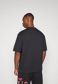 Svart t-skjorte med korte ermer og rund hals, laget av glatt stoff, har en avslappet passform og minimalistisk design.