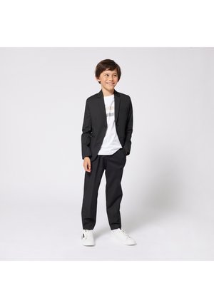 Svart pinstripe drakt med skreddersydd jakke og matchende bukser, kombinert med en hvit grafisk t-skjorte og hvite joggesko.
