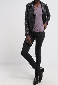 Giacca da motociclista in pelle nera sopra un top lavanda, abbinata a jeans skinny neri e stivaletti. Texture liscia, design aderente e linee eleganti.