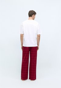 T-shirt en coton blanc à manches courtes, associé à un pantalon en flanelle à carreaux rouges, avec des jambes larges et une texture douce.