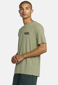 T-shirt z krótkim rękawem w kolorze oliwkowym, wykonany z miękkiego materiału, z czarnym logo nadrukowanym z przodu i luźnym krojem.