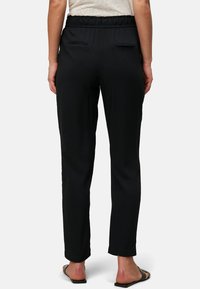 Schwarze Hose mit elastischem Bund, zwei Gesäßtaschen und geradem Bein-Design. Glatter Stoff und minimalistische Details.