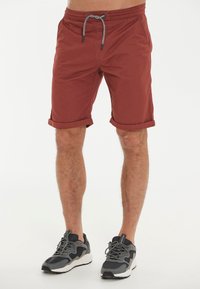 Röda shorts med dragsko i midjan och uppvikta fållar. Lättviktsmaterial med en slät textur. Bärs med grå och svarta träningsskor.