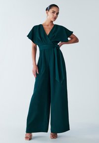 Teal jumpsuit with short flutter sleeves, a V-neckline, and a tied waist, featuring wide legs and a flowing fabric texture.