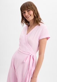 Wikkeljurk in lichtroze, gemaakt van gestructureerde stof. Korte mouwen, V-halsontwerp en een gestrikt taille-detail versterken het casual uiterlijk.