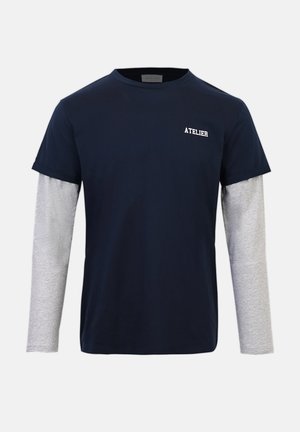 Navy blue short-sleeve T-shirt layered over light gray long sleeves, with "ATELIER" text on the left chest.